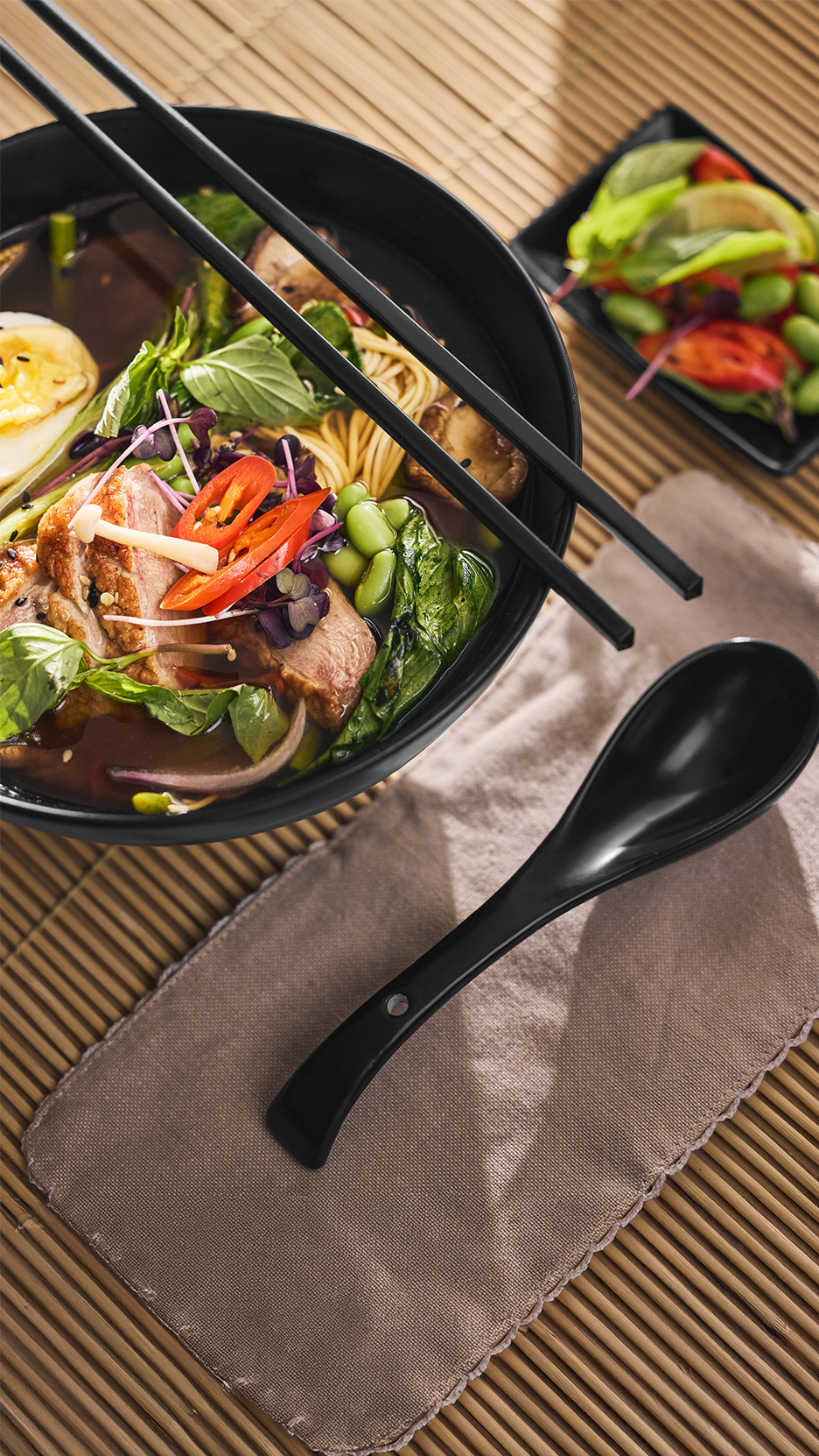 Bol de ramen cu rață, tăiței, legume și ou, cu bețișoare și lingură.