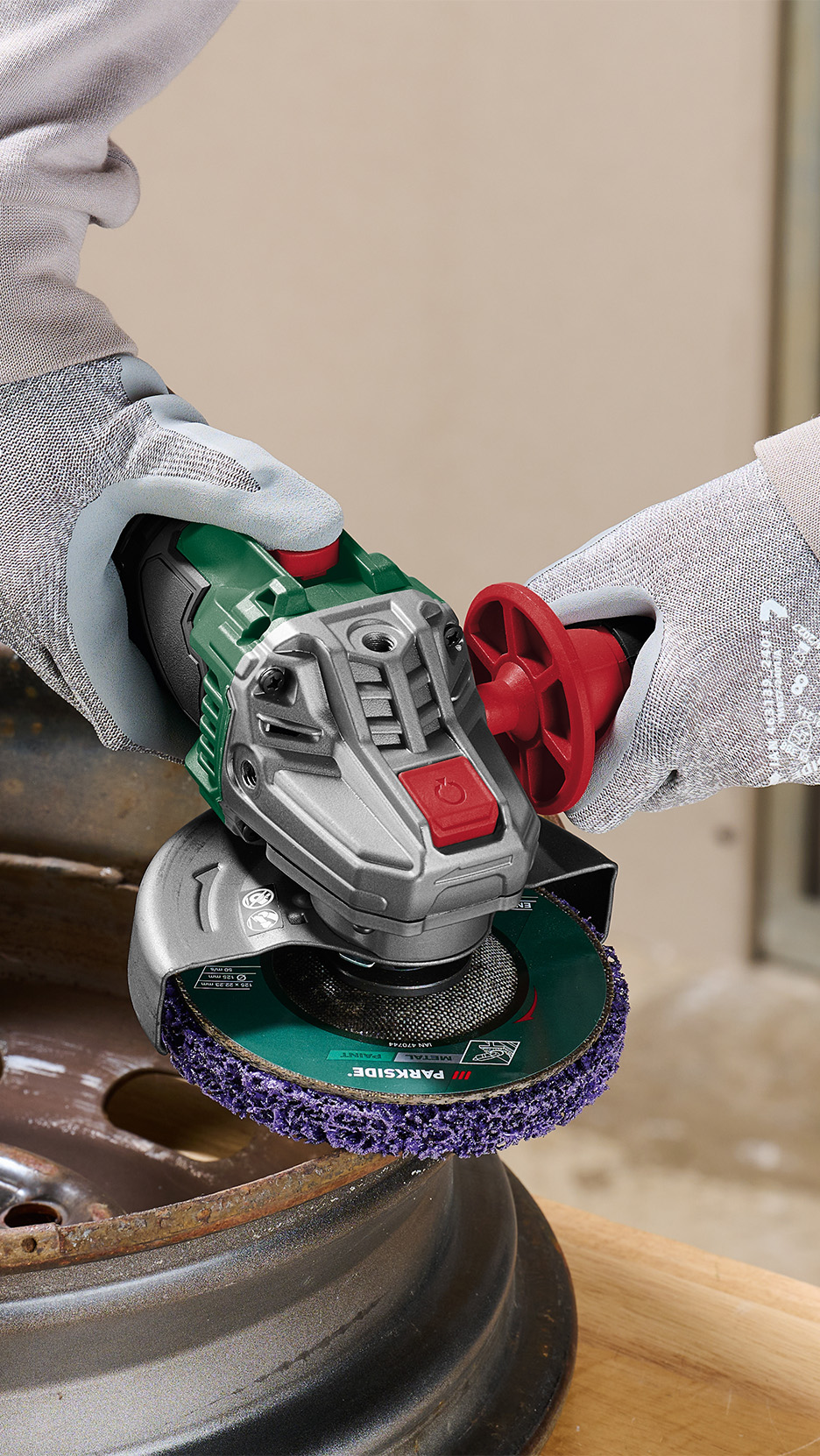 O persoană folosește un polizor unghiular cu un disc de curățare violet pe o jantă metalică ruginită.