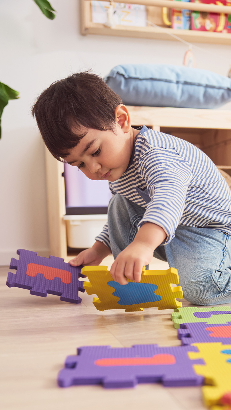 Un copil se joacă pe podea cu piese de puzzle colorate din spumă.