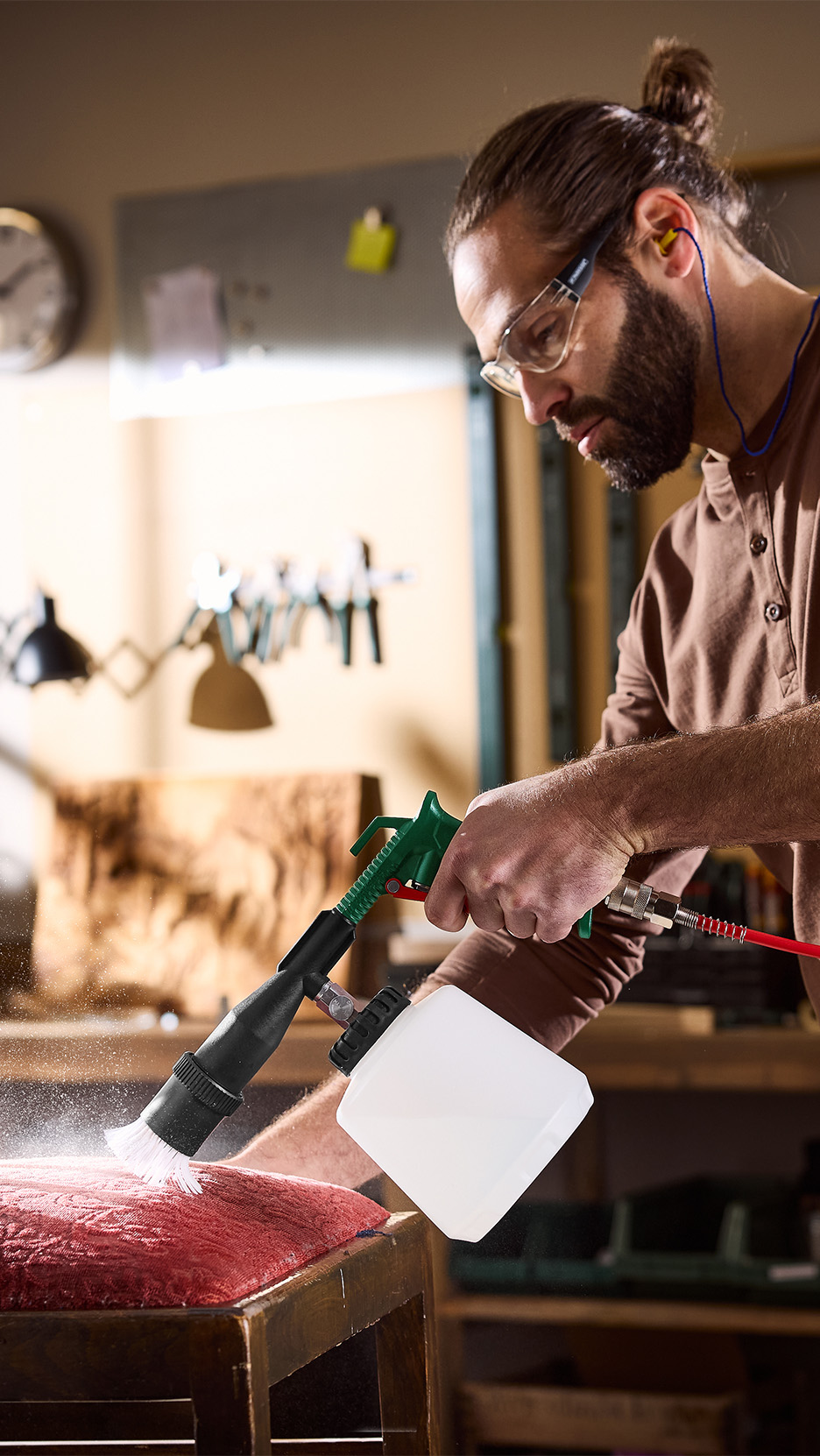 Bărbat care curăță o tapițerie roșie cu un pistol de curățare cu aer comprimat.