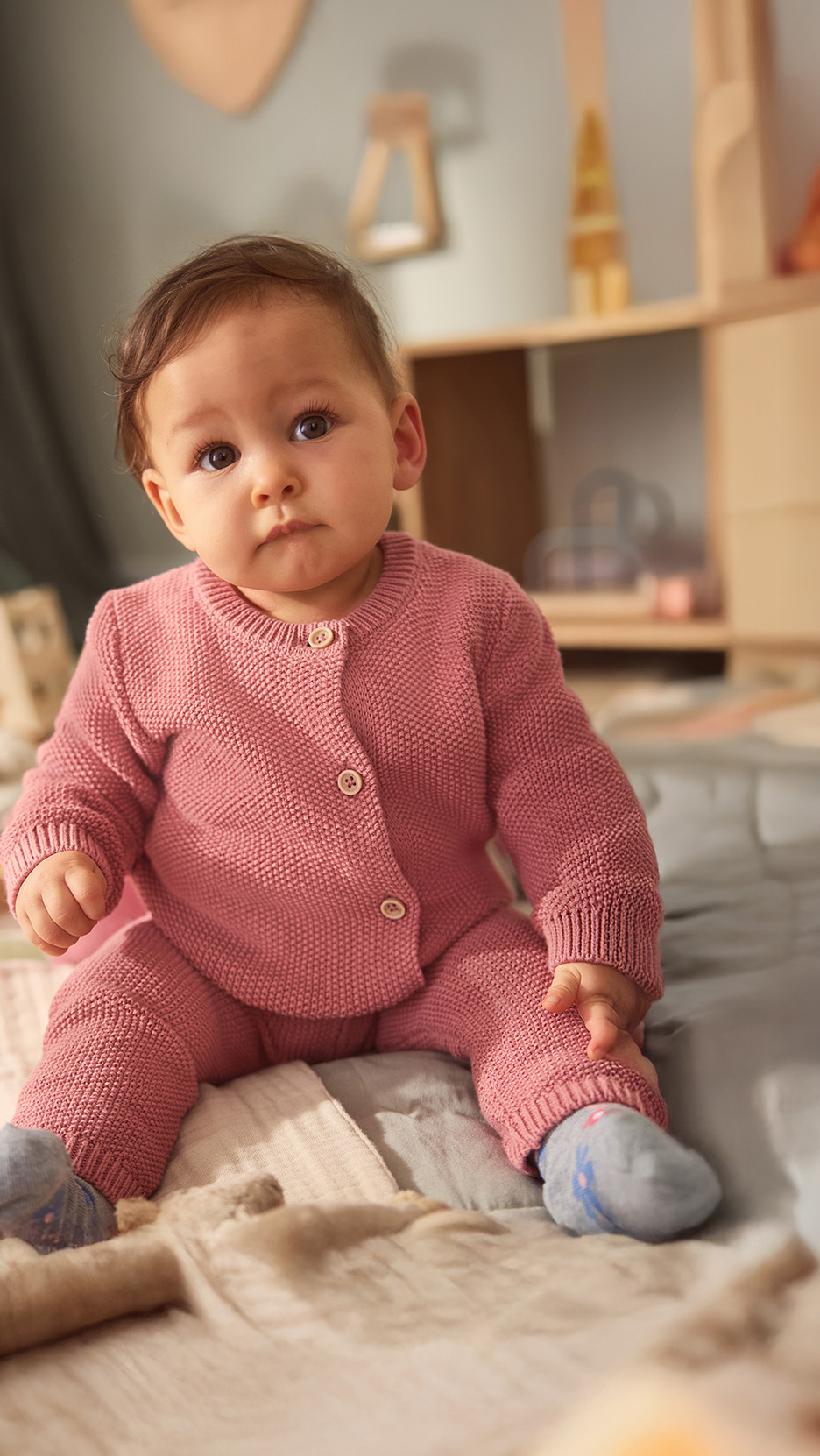 Bebeluș drăguț într-un set tricotat roz, șezând pe o pătură moale.