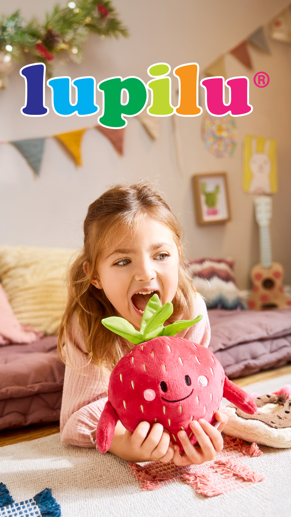 Fetiță zâmbitoare cu o jucărie de pluș căpșună, cu textul „lupilu” deasupra.