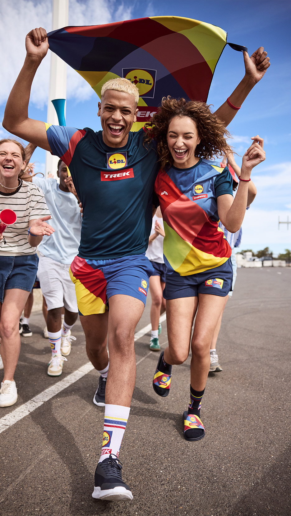 Doi tineri fericiți poartă tricouri și pantaloni scurți sportivi cu modele colorate, alergând cu un steag.