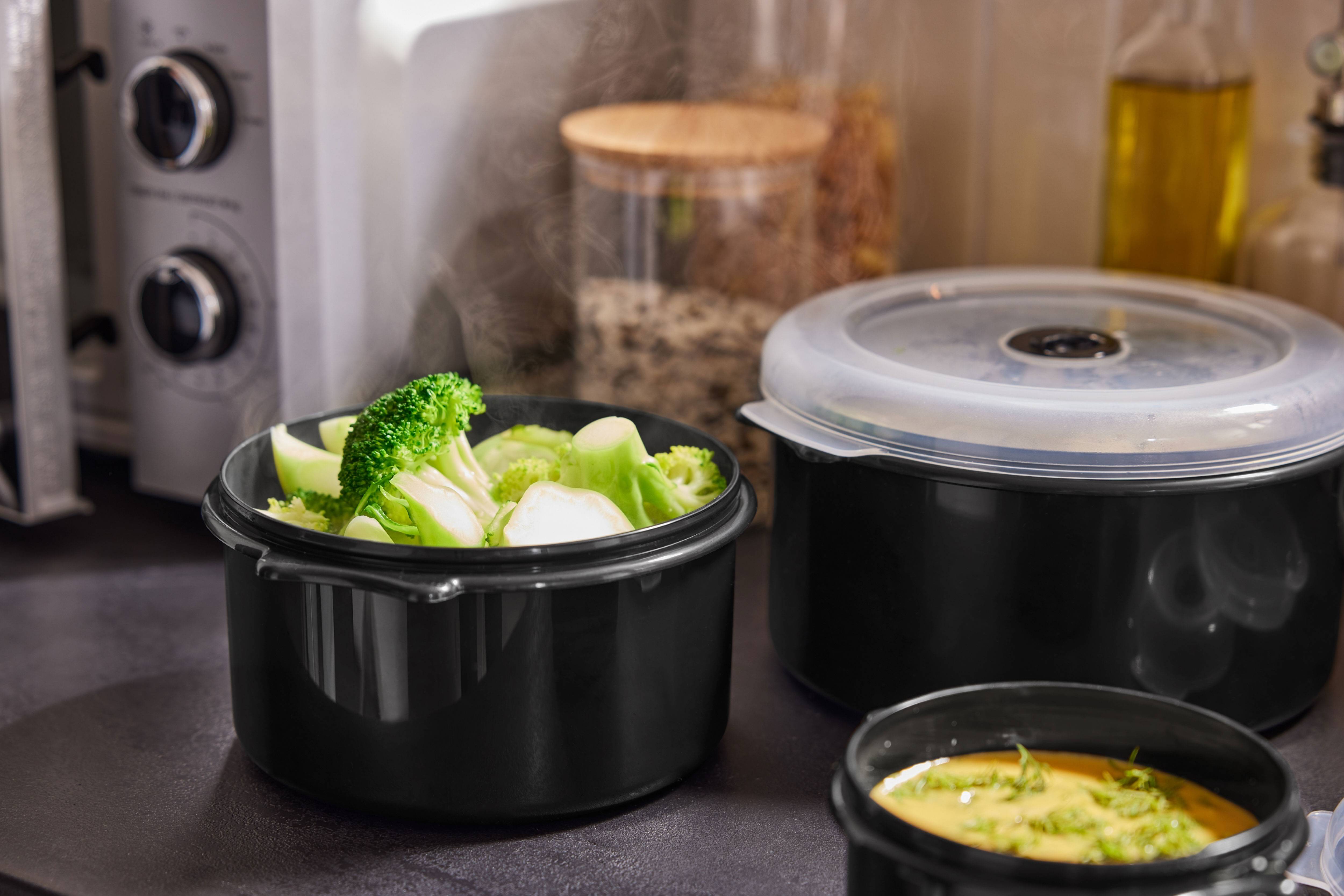 Broccoli aburind și alte mâncăruri în recipiente negre pe blatul de bucătărie.