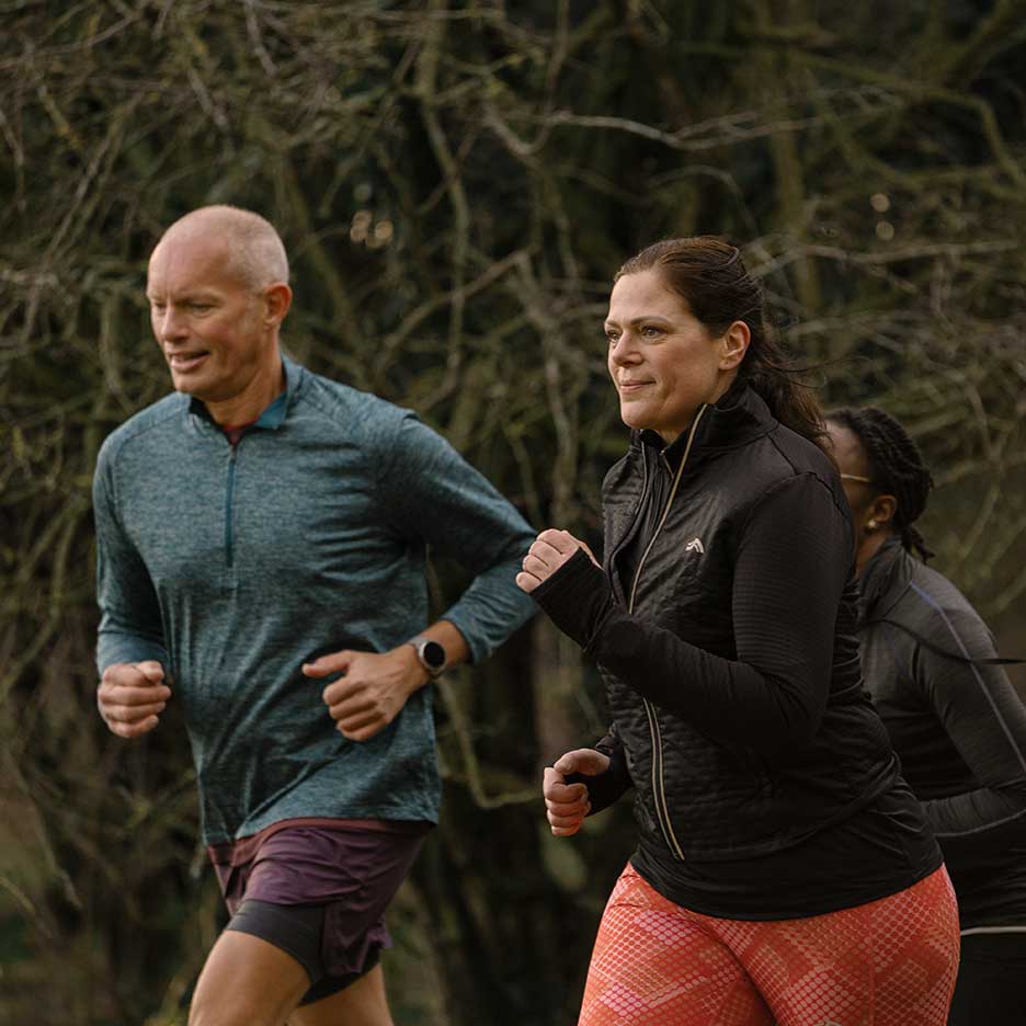 Doi alergători adulți în echipament sportiv fac jogging în aer liber.