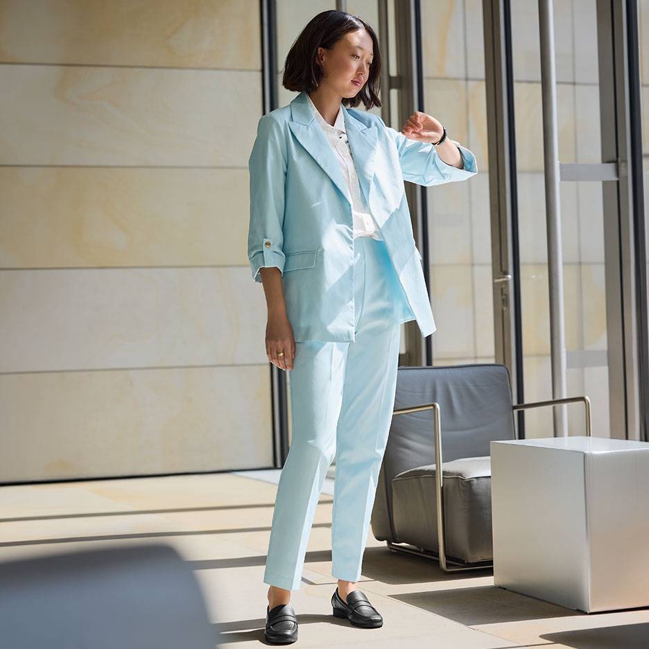 Femeie în costum bleu deschis, cu sacou și pantaloni, purtând mocasini negri.