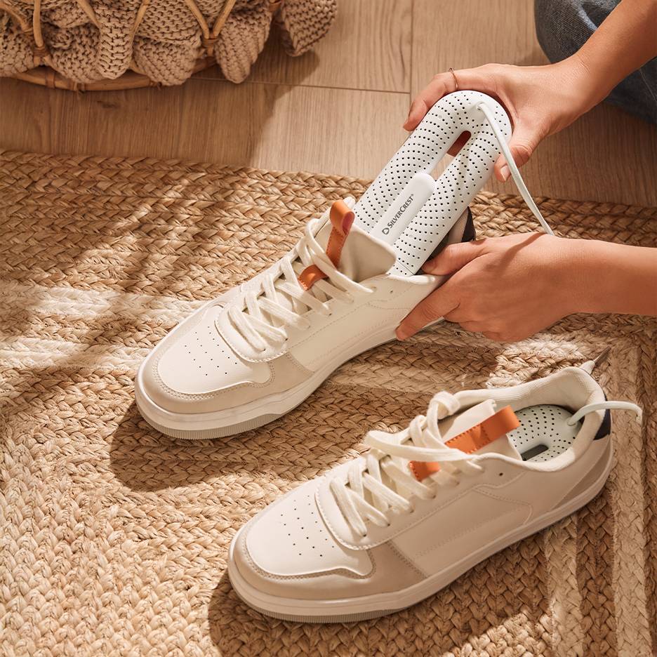 Uscător de pantofi Silvercrest în adidași albi pe un covor împletit.