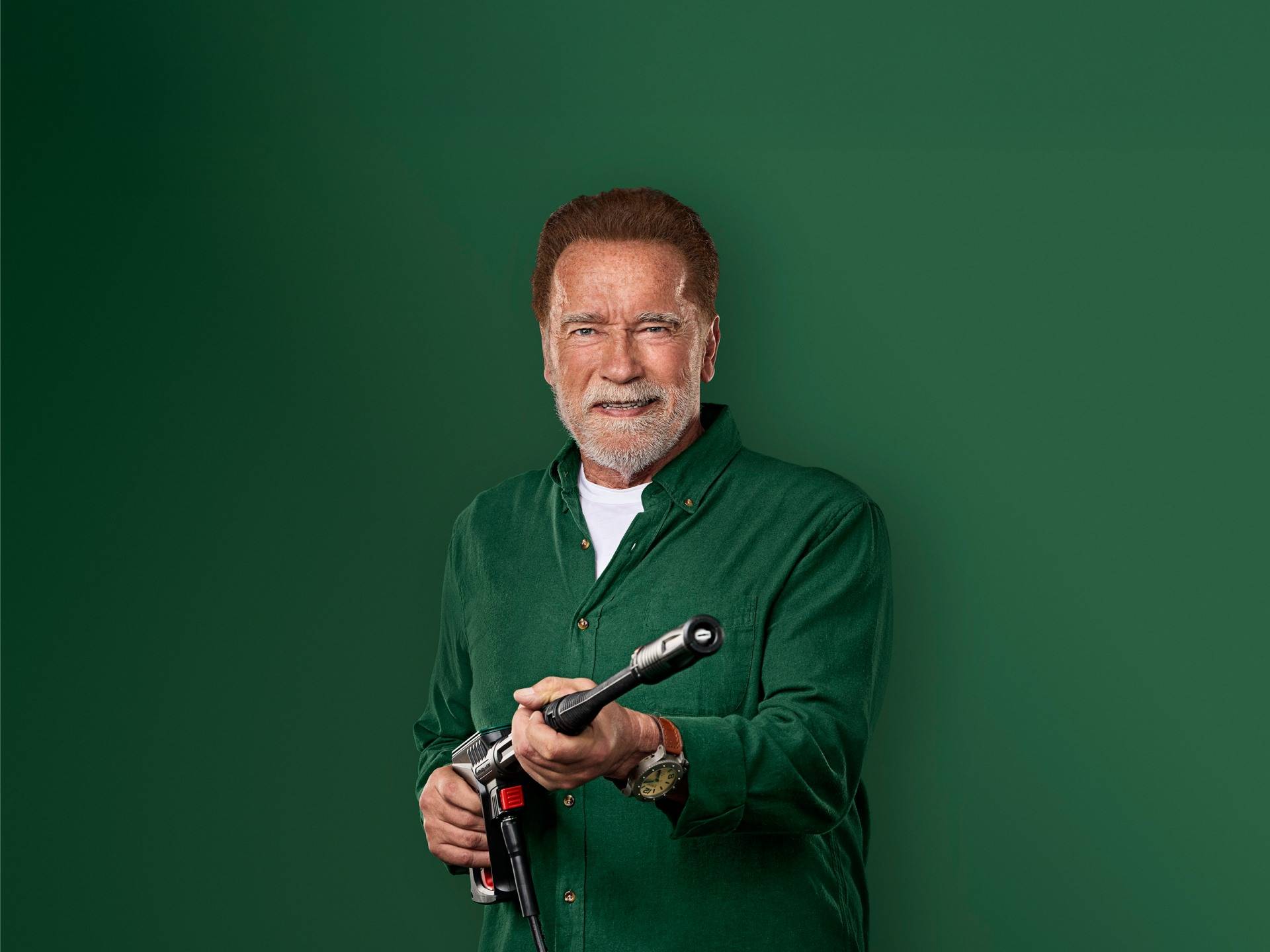 Arnold Schwarzenegger zâmbește, ținând un pistol de spălare cu presiune.