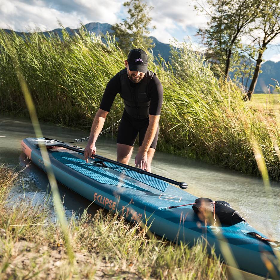 Bărbat în costum de neopren negru pregătindu-se pentru paddleboard, placă în apă