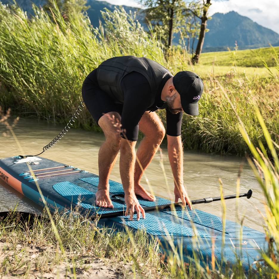 Bărbat în costum de neopren și vestă de salvare, pregătindu-se pentru stand-up paddle pe râu.
