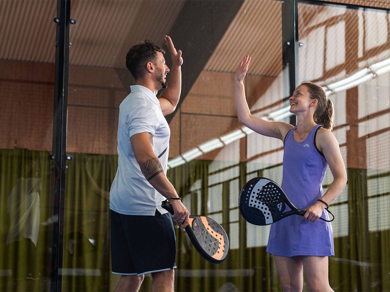 Doi jucători de padel, un bărbat și o femeie, își dau un high-five pe teren.