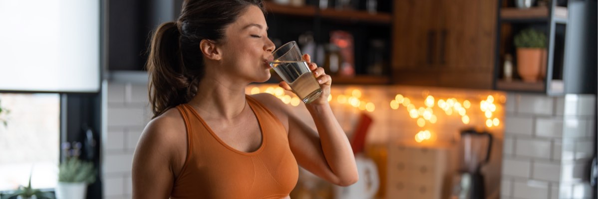 Femeie în sutien sport bea apă în bucătărie.