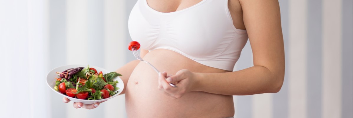 Femeie gravid mănâncă o salată sănătoasă.
