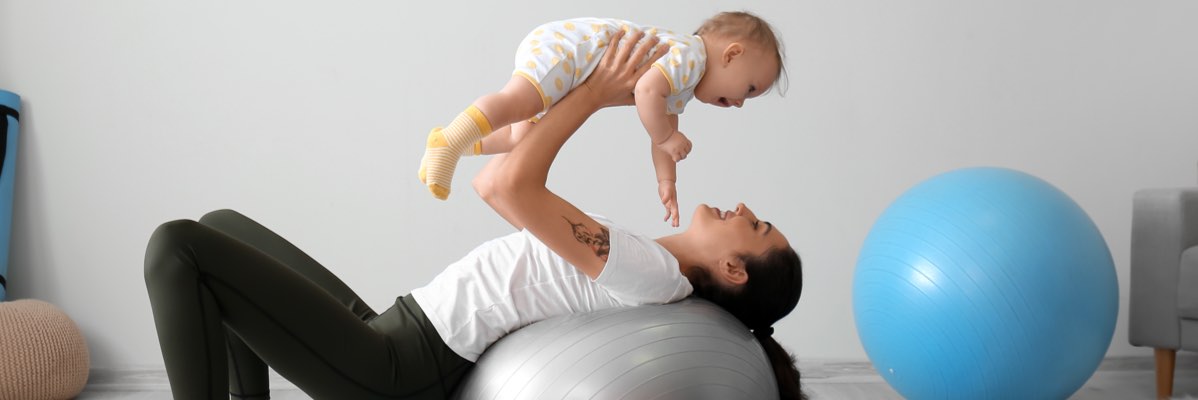 Mamă face exerciții cu bebelușul și minge de pilates.