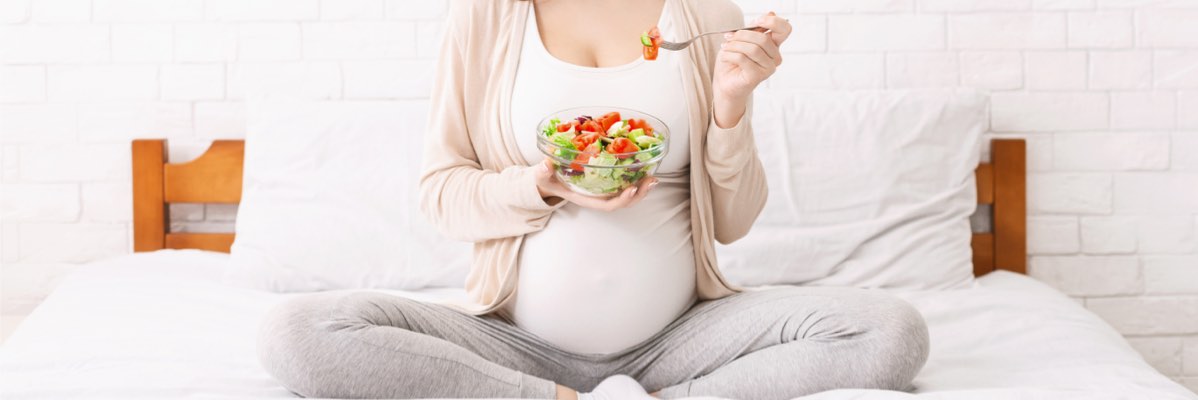 Femeie însărcinată mănâncă o salată sănătoasă în pat.