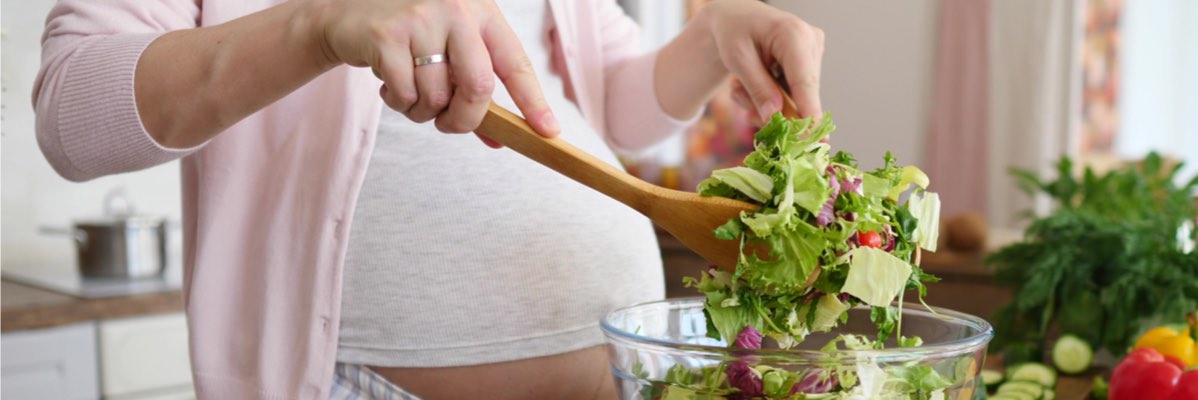 Femeie însărcinată prepară o salată.