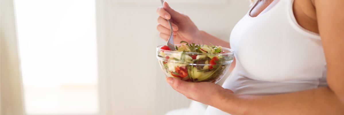 O femeie însărcinată mănâncă o salată proaspătă.