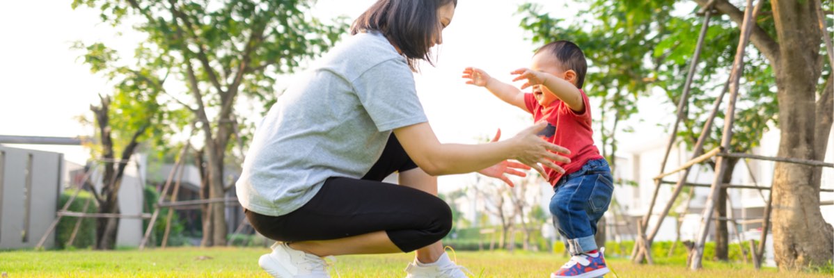 O mamă ajută copilul ei să facă primii pași într-un parc.