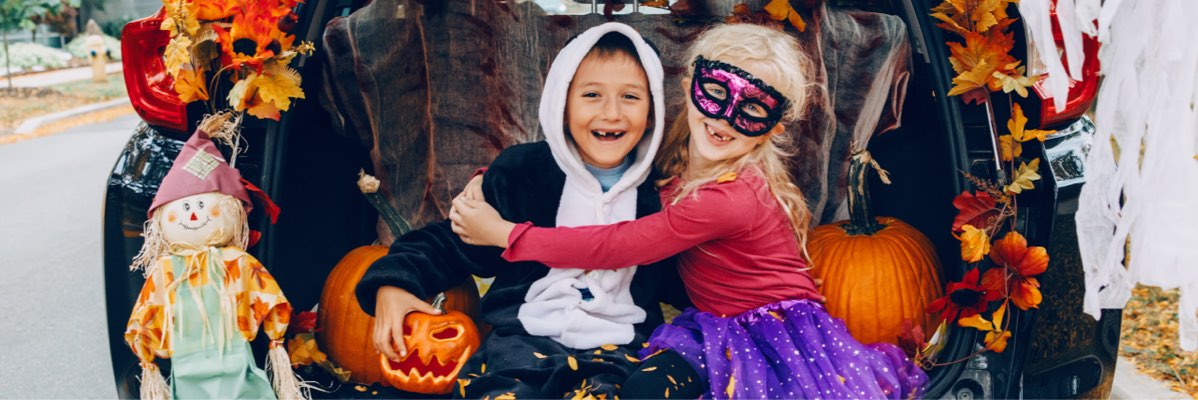 Copii în costume de Halloween cu dovleci în portbagajul mașinii.