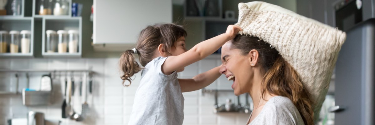O fetiță se joacă cu o pernă cu mama ei în bucătărie.