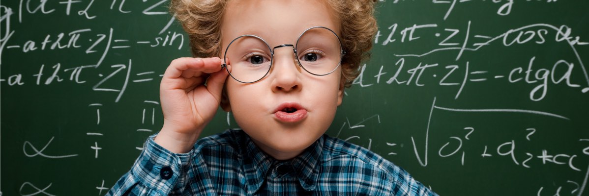 Băiat cu ochelari în fața unei table cu formule matematice.