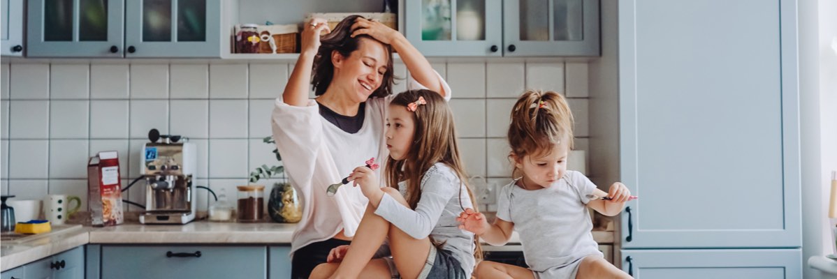 Mama și două fiice iau micul dejun în bucătărie.
