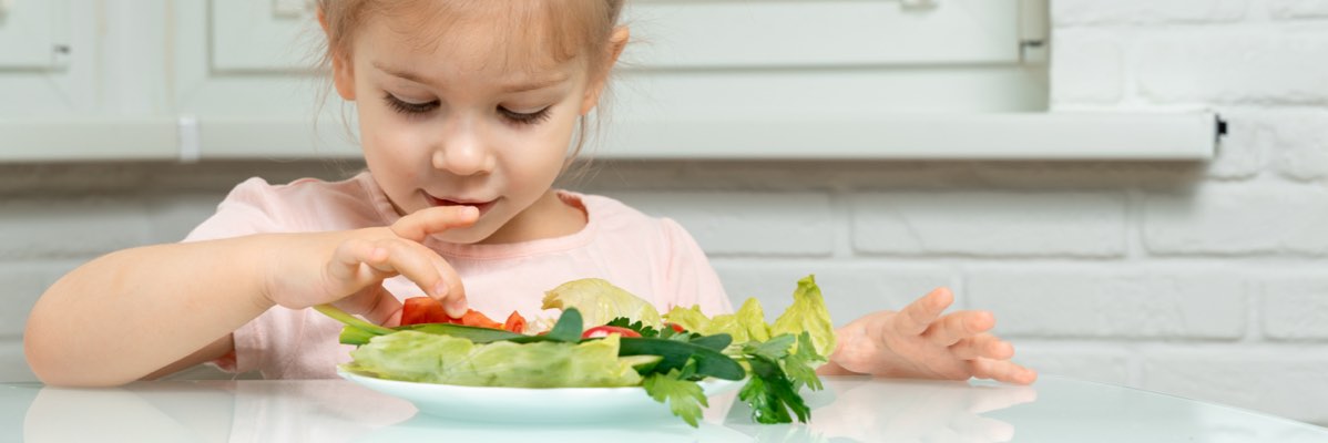 O fetiță mică mănâncă o salată cu diferite legume.