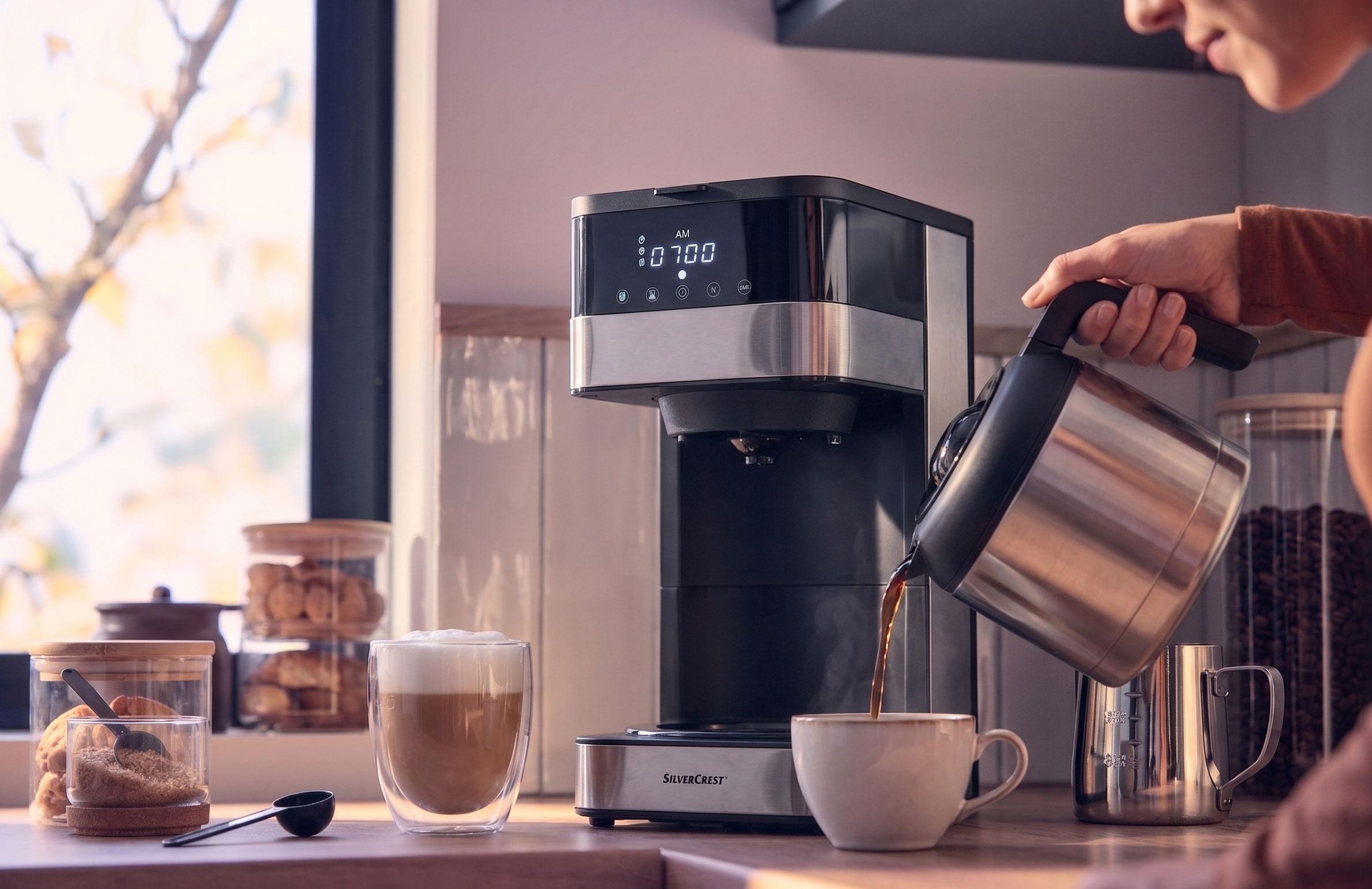 Aparat de cafea turnând cafea într-o ceașcă, cu un latte și prăjituri pe blat.