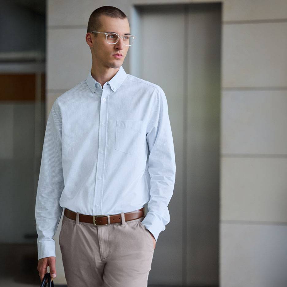 Bărbat în cămașă albastru deschis cu dungi și pantaloni bej cu curea maro.