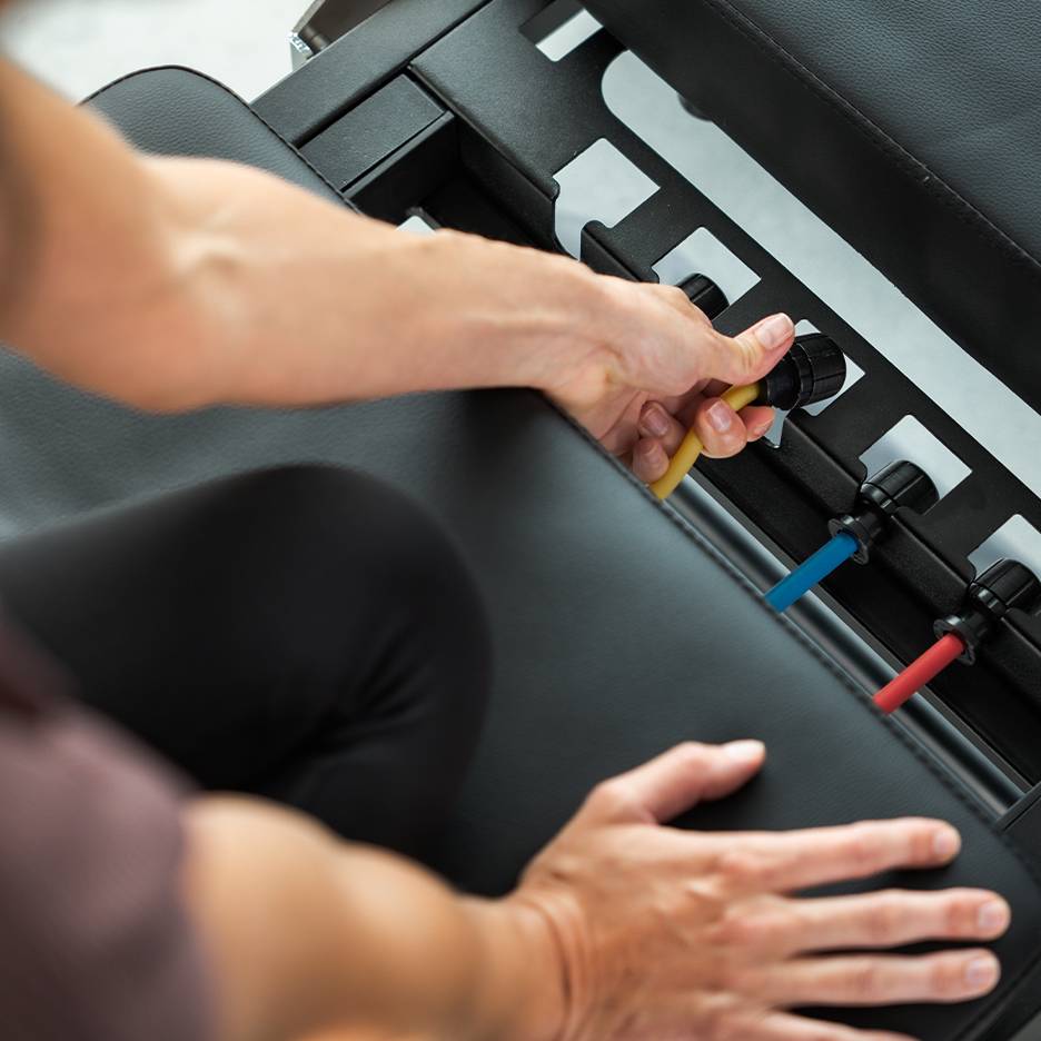 Persoană ajustând benzi de rezistență pe o bancă de exerciții.