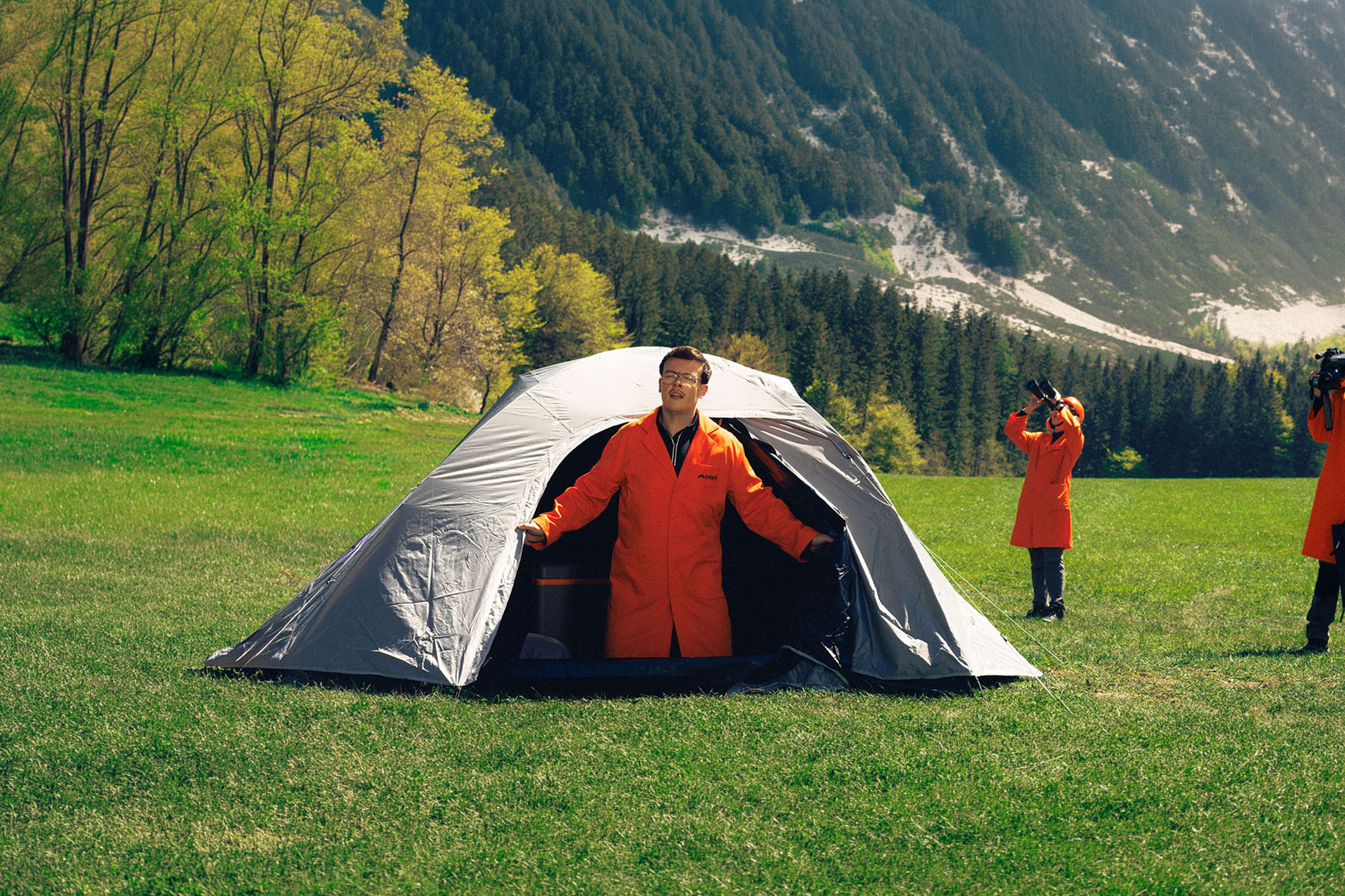 Generat de AI: Trei persoane în halate portocalii cu echipament de camping și observare pe o pajiște.
