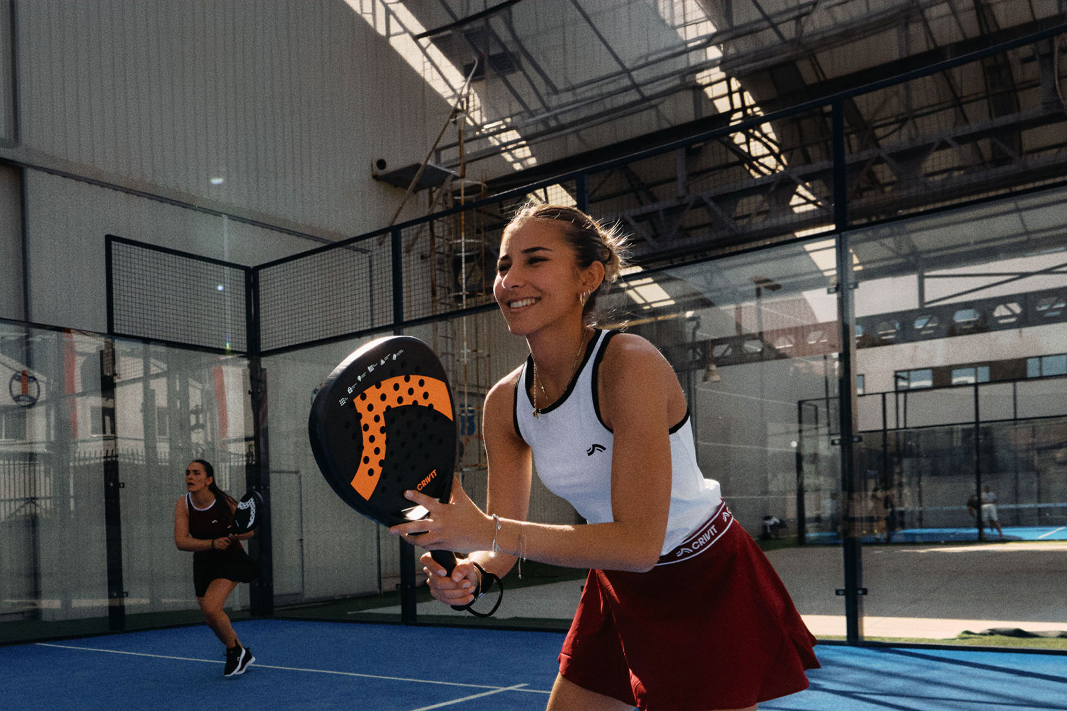 Generat de AI: Două femei jucând padel tenis, una zâmbind și ținând o rachetă, pe un teren albastru.