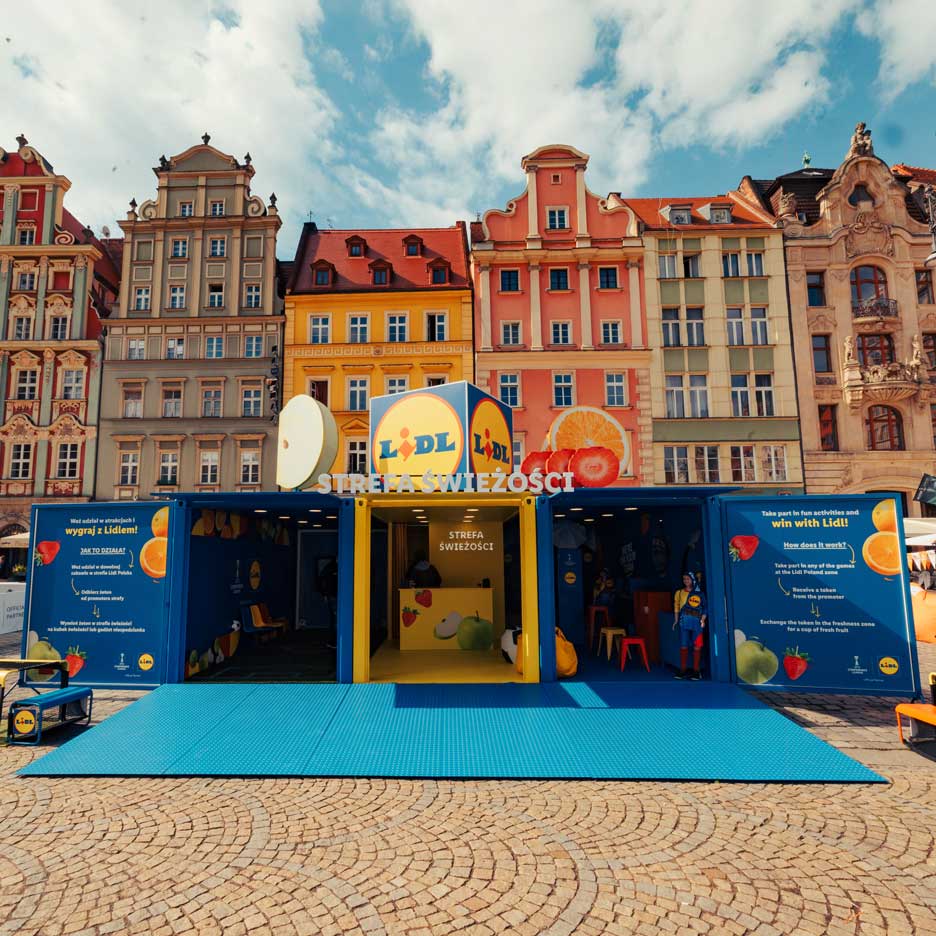 O instalație Lidl cu tematică de fructe și legume, cu jocuri și activități, pe o piață urbană.