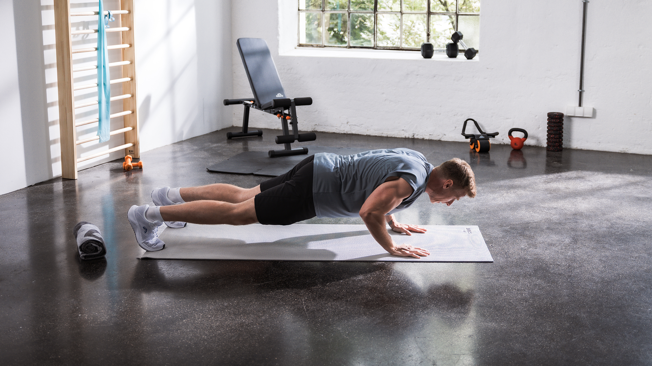 Bărbat făcând flotări pe o saltea într-o sală de sport acasă cu diverse echipamente de fitness.
