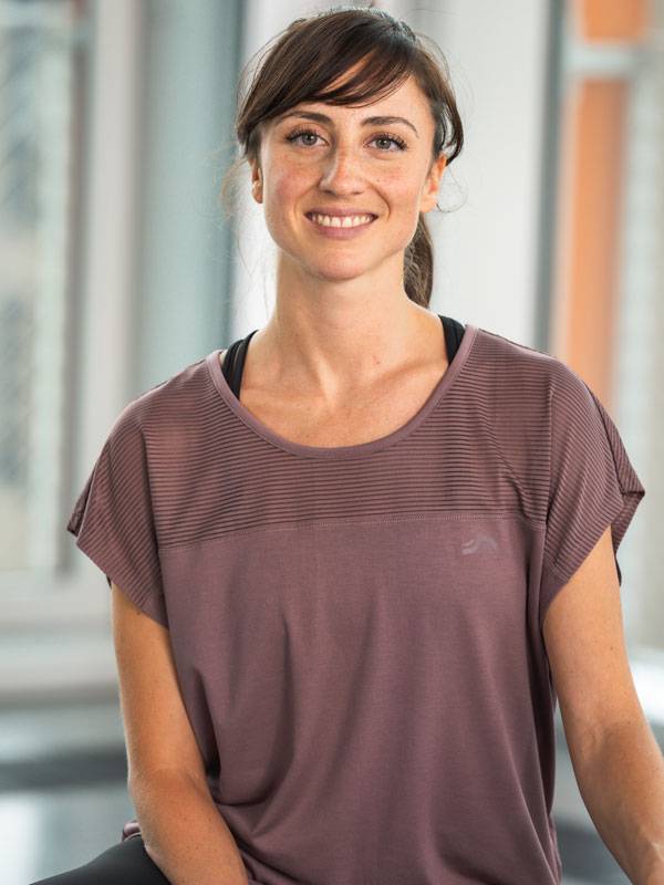 Femeie zâmbitoare purtând un top sportiv mov cu mânecă scurtă.