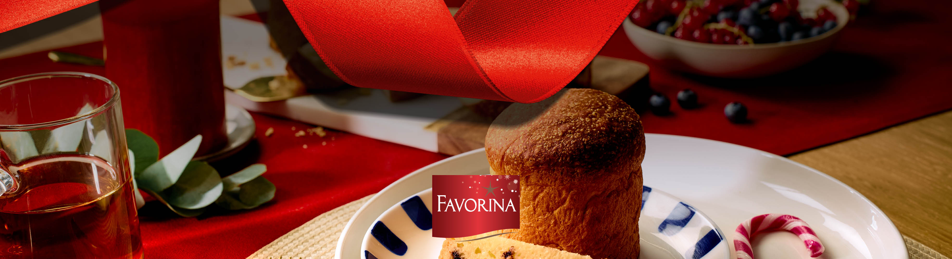 Panettone Favorina pe o masă festivă cu fructe de pădure și o băutură.