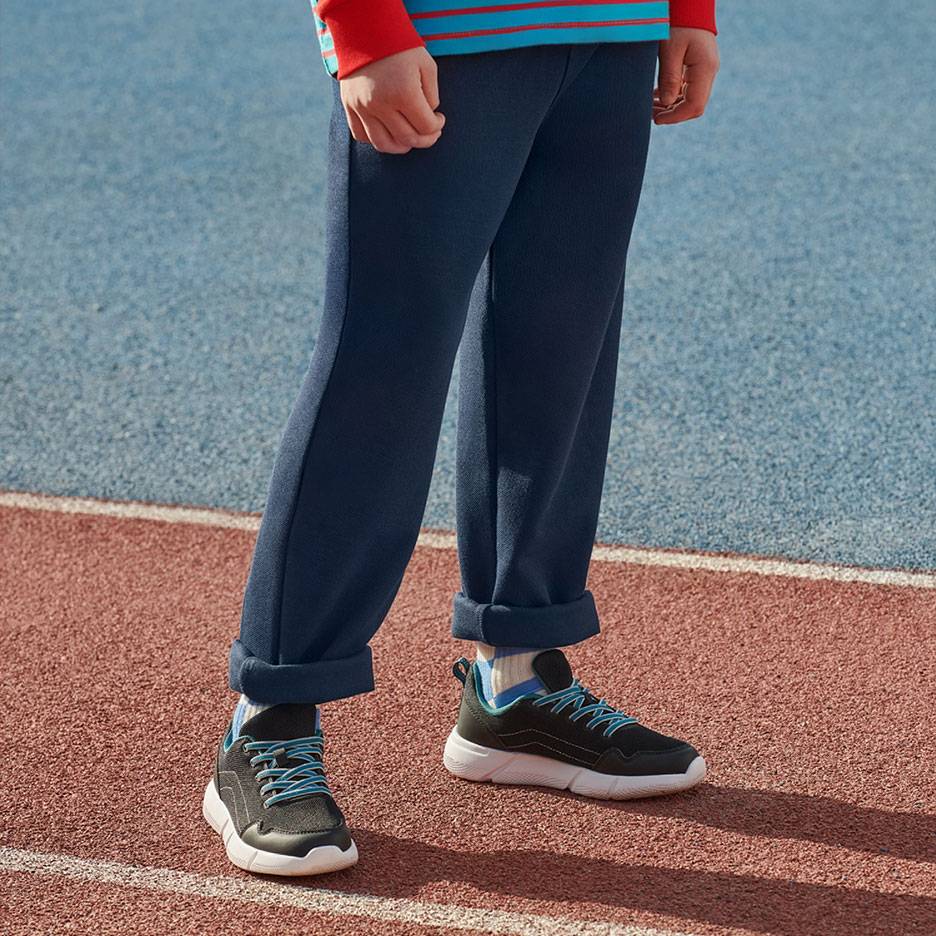 Pantaloni de trening bleumarin și adidași negri cu șireturi albastre pe o pistă de alergare.
