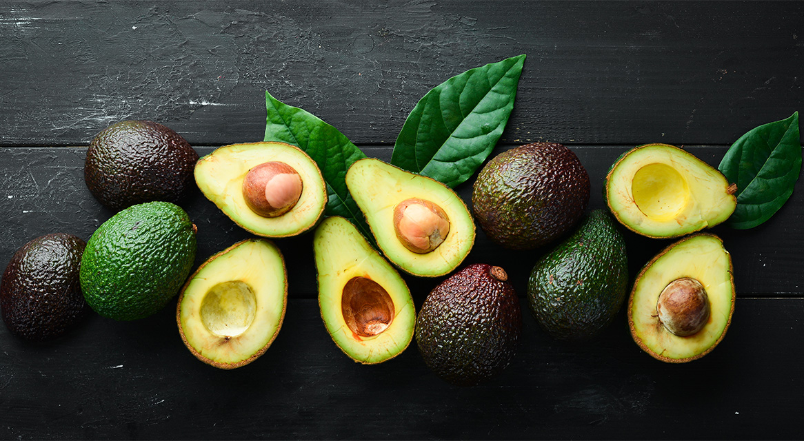 Avocado tăiate și întregi pe o suprafață de lemn negru.