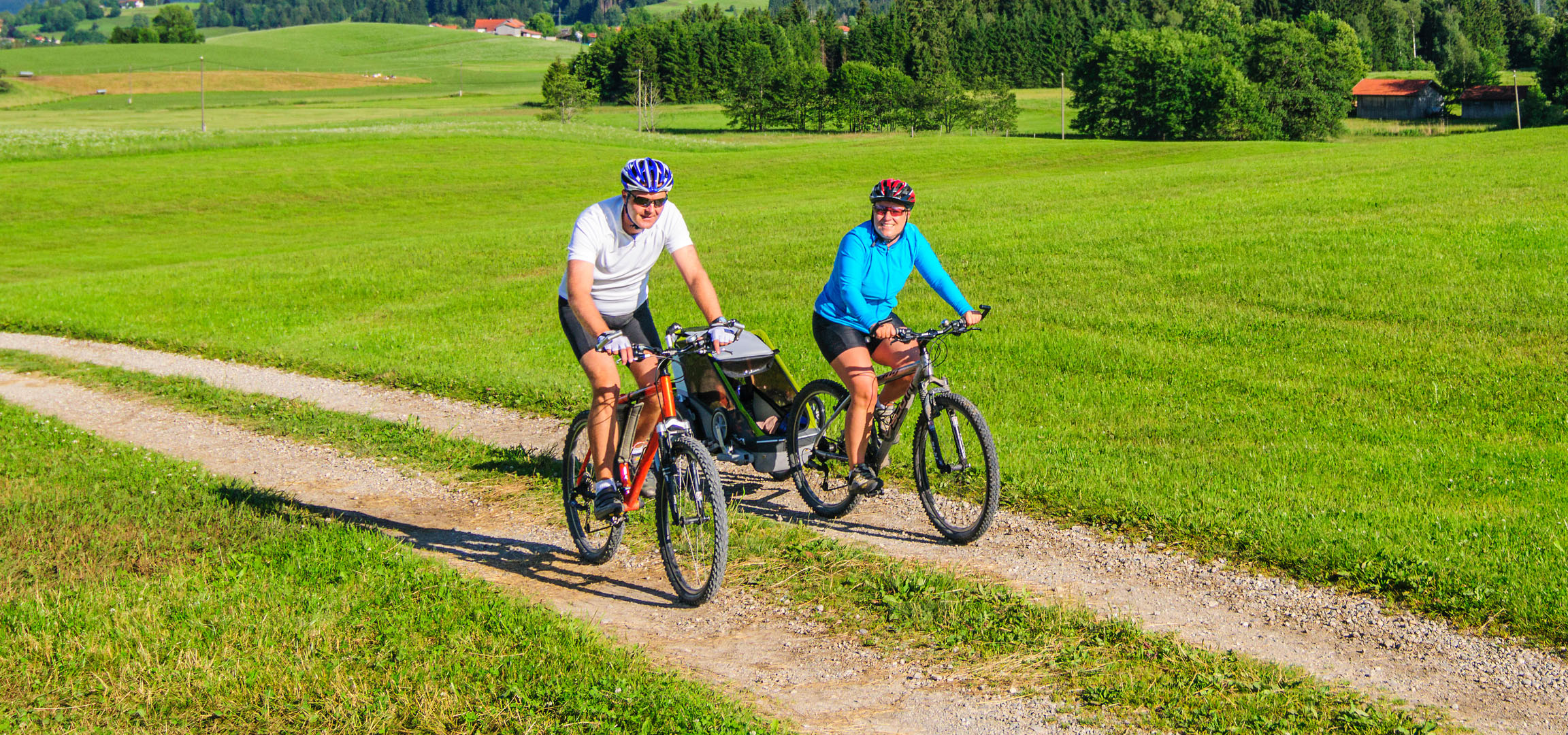 Cuplu care merge cu bicicleta într-un peisaj verde.