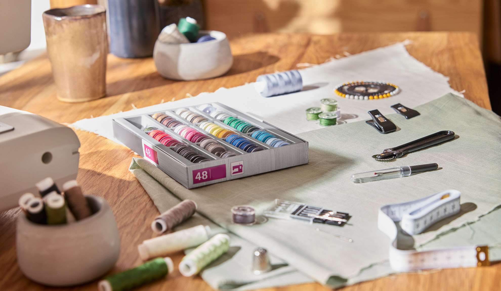 Set de cusut cu o cutie de ațe colorate, mașină de cusut și diverse unelte pe o masă de lemn.