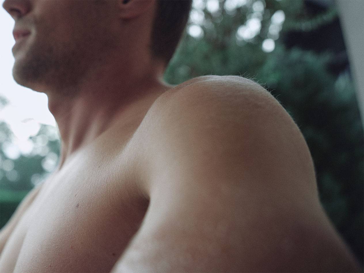 Prim-plan cu umărul și gâtul unui bărbat, cu un fundal verde estompat.