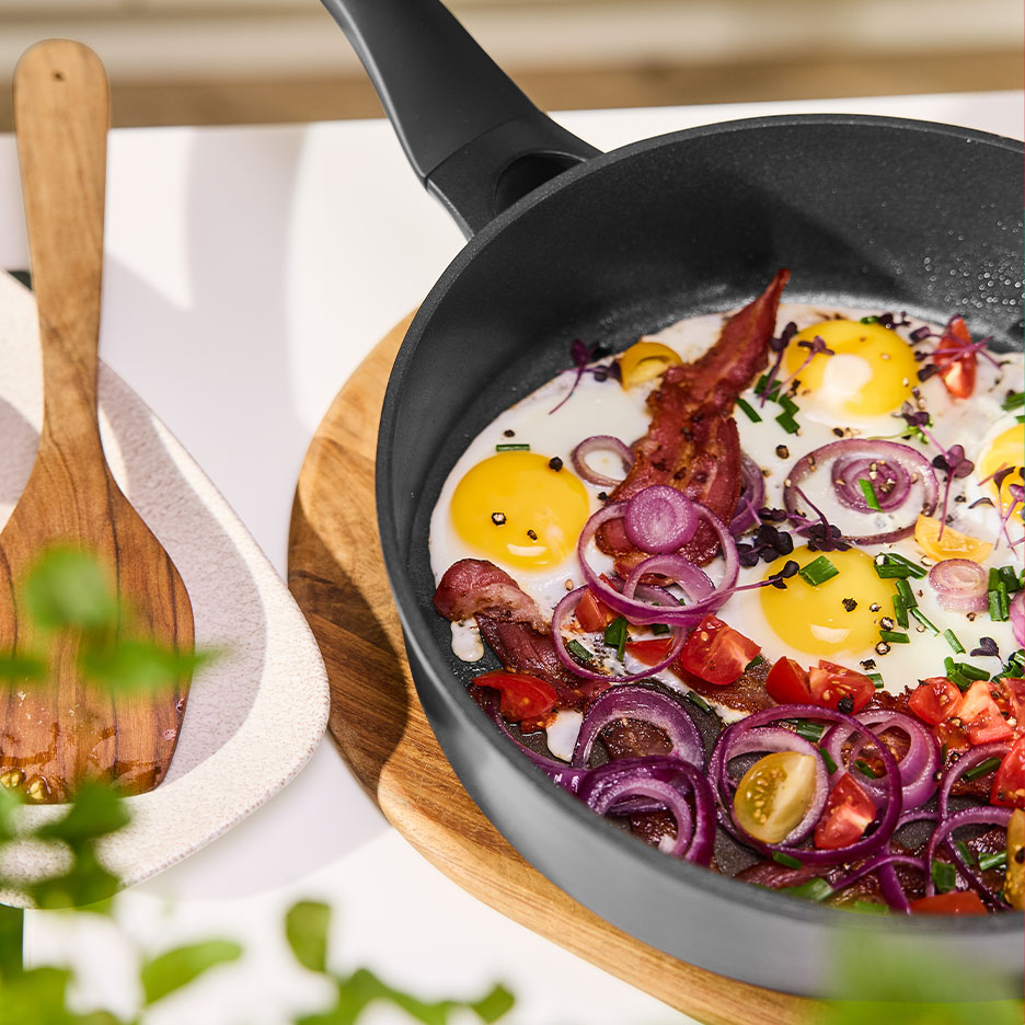 Tigaie cu ouă prăjite, bacon, ceapă roșie și roșii.