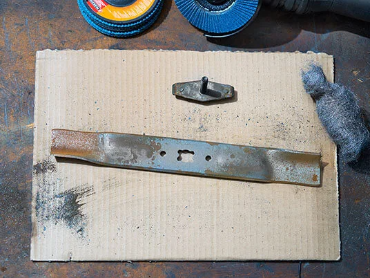 Lamă de mașină de tuns iarba ruginită pe carton cu discuri abrazive și lână de oțel.