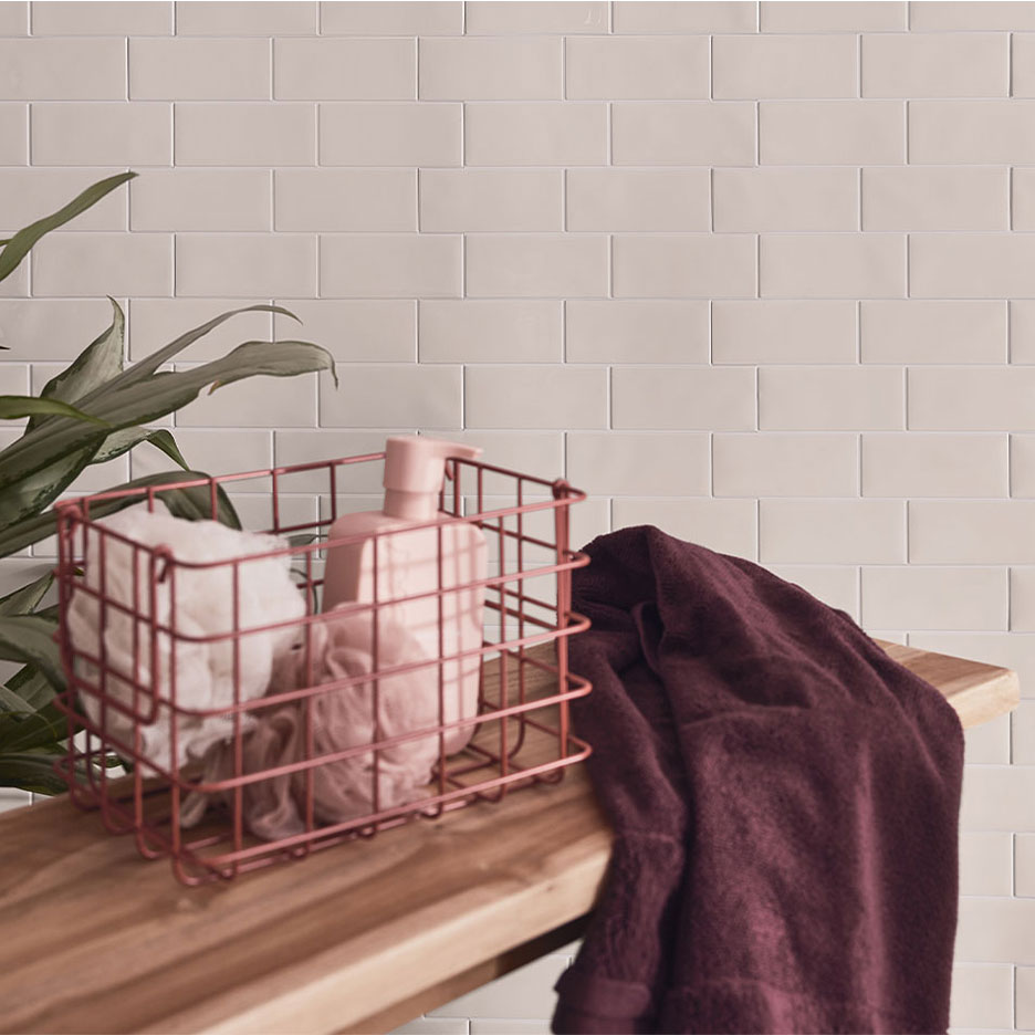 Decor de baie cu gresie albă, bancă de lemn, coș cu săpun și prosoape.