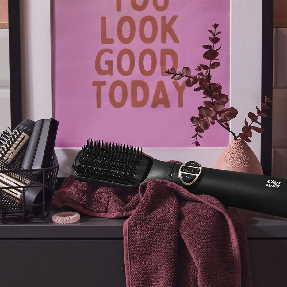Perie de îndreptat părul Cien Beauty pe un prosop, cu accesorii de păr și un poster.