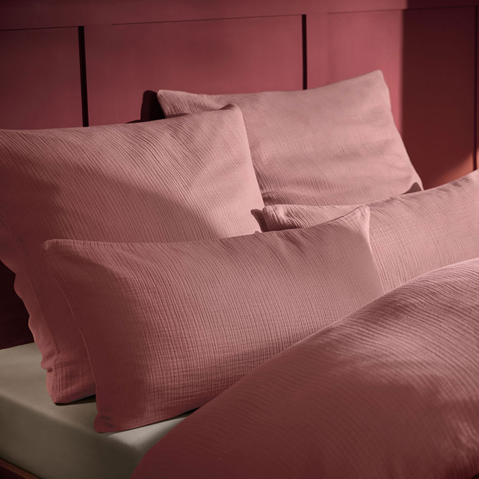 Pernă și lenjerie de pat roz din muselină pe un pat cu tăblie din lemn.