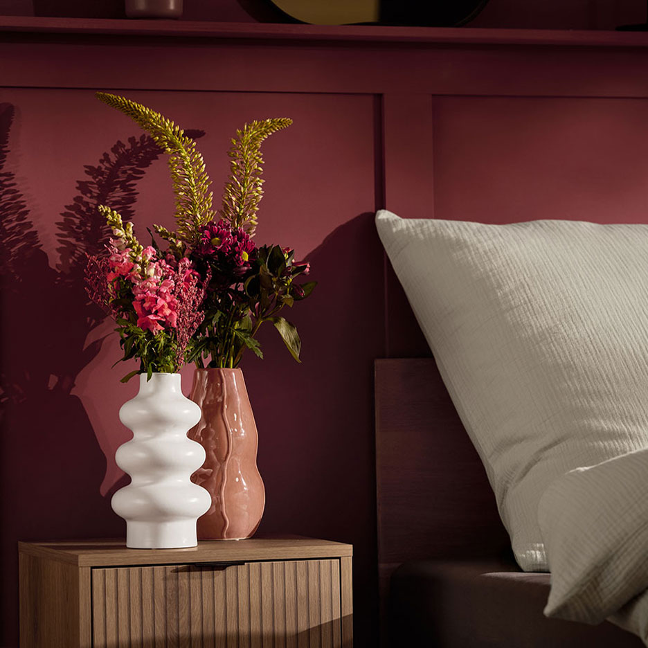 Două vaze cu flori pe o noptieră lângă un pat cu o pernă albă.