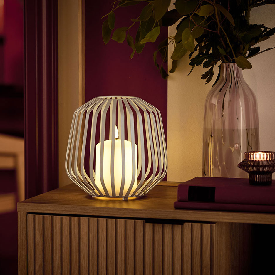 O lumânare LED într-un suport metalic alb, pe o comodă din lemn.