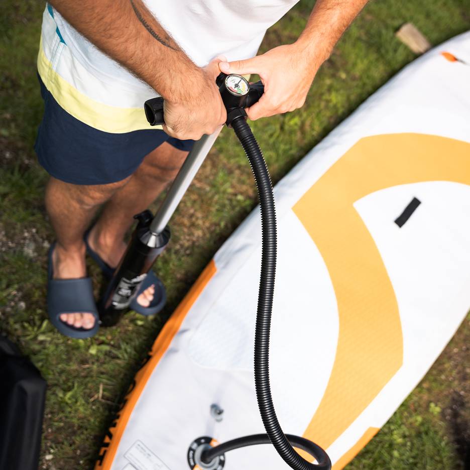 Bărbat umflând o placă de paddleboard gonflabilă cu o pompă manuală.