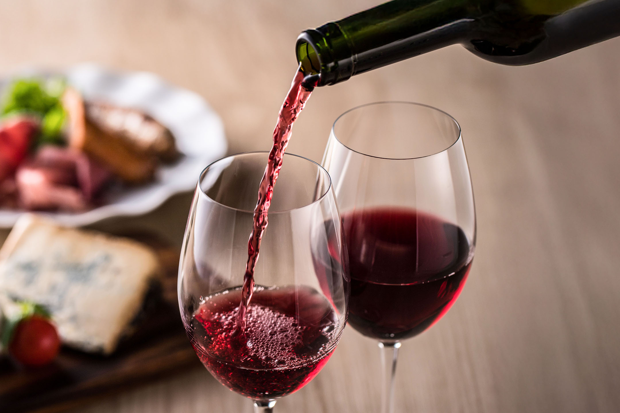 Vin roșu turnat într-un pahar, cu aperitive în fundal.